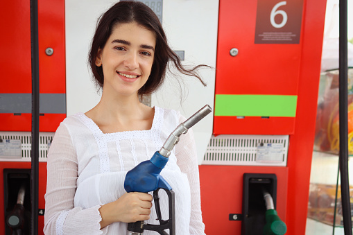 Portrait of happy smiling customer woman holding fuel petrol pump nozzle against for filling up her car, beautiful young lady traveler self refueling car with petrol at self-service gas station.