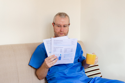 Candid image of a male medical worker wearing scrubs in a home environment, performing a range of different activities.