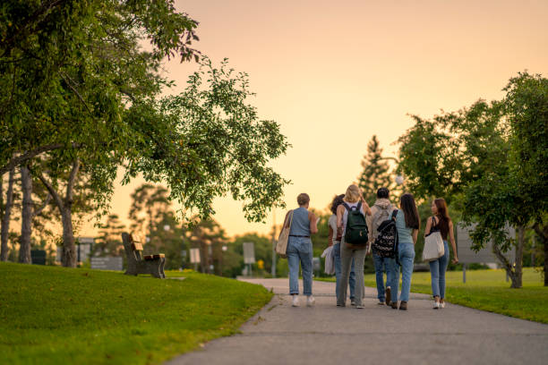 University Students Walking Outside on Campus A group of University students are seen from behind walking outside on campus as they make their way to class.  They are dressed casually and have backpacks on as they talk together and make their way to school for the day. university student stock pictures, royalty-free photos & images