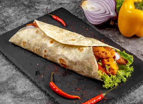 Hot and Spicy shawarma Wrap served in a cutting board on grey background side view of fastfood
