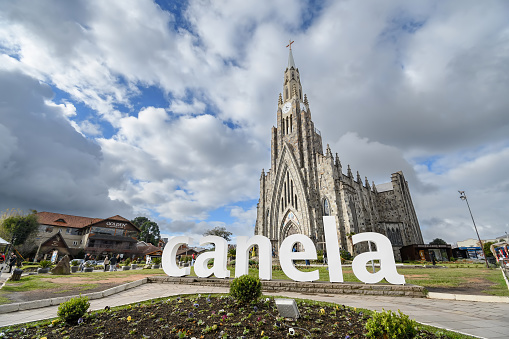 Canela, RS, Brazil - May 19, 2022: the city name totem in front of the Stone Cathedral, Catedral de Pedra in portuguese. The Nossa Senhora de Lourdes church at the Matriz Square.