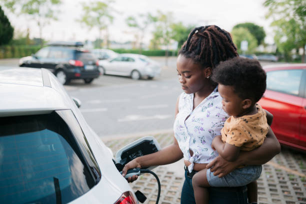 Mother holding her son while charging her electric vehicle stock photo