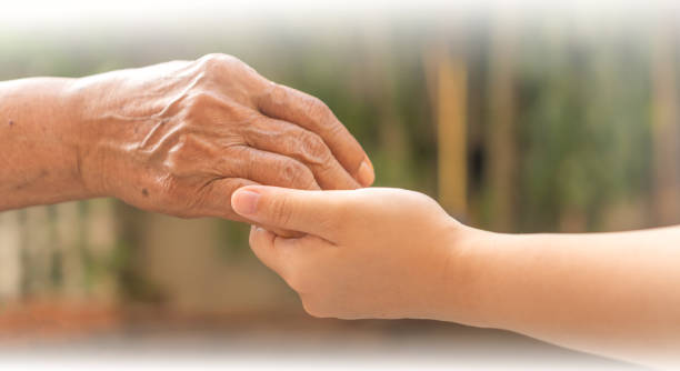 starsza kobieta trzymająca za rękę młodego opiekuna w domu opieki. opiekun trzyma starszą rękę w opiece hospicyjnej. filantropijna życzliwość dla niepełnosprawnej koncepcji. - one week old zdjęcia i obrazy z banku zdjęć