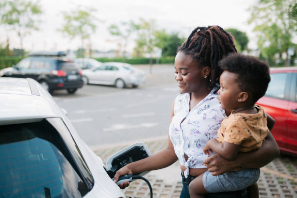 madre sosteniendo a su hijo mientras carga su vehículo eléctrico - vehículo eléctrico fotografías e imágenes de stock