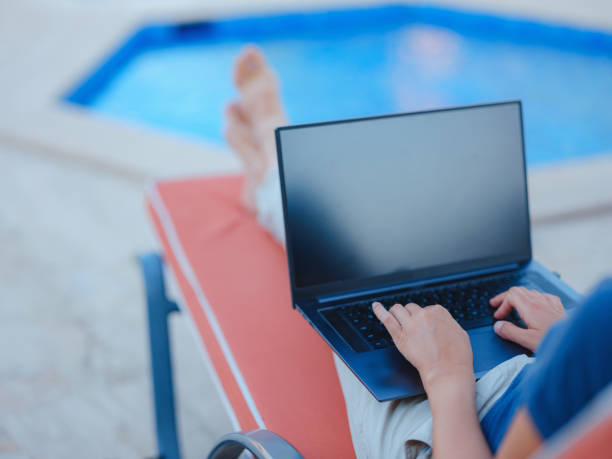 istock Young business woman working at computer by hotel pool. 1412462708