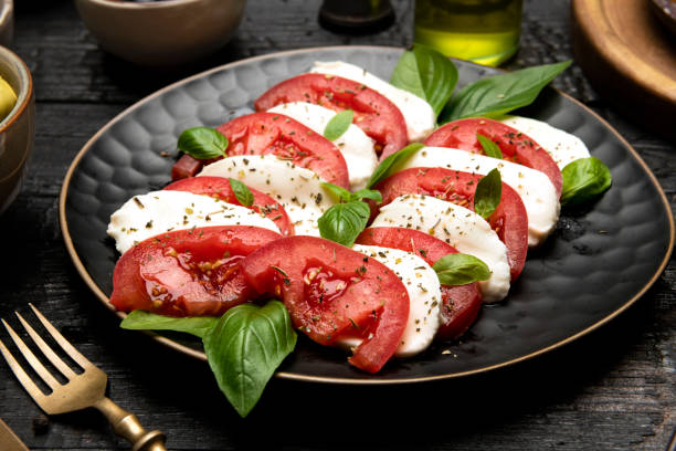 Caprese salad with mozzarella, tomatoes, and basil Vegetarian food. Caprese salad with mozzarella, tomatoes, and basil served on dark plate on dark background caprese salad stock pictures, royalty-free photos & images