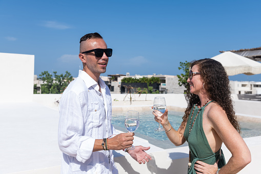 This is a photograph of a white couple in their early 40s drinking water on the rooftop by the side of the pool while in Mexico for summer vacation.