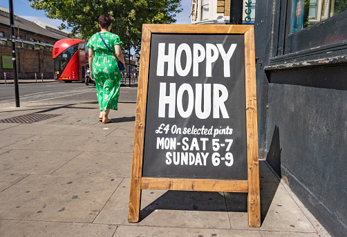 A woman walks past the Happy Hour Sign at The Lock Tavern on Chalk Farm Road in Chalk Farm, London