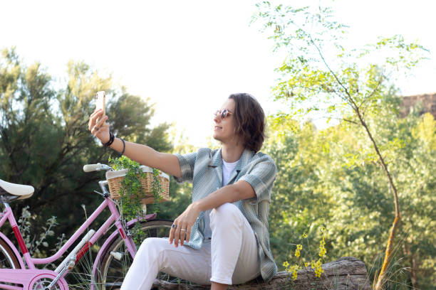 istock Young handsome man taking a selfie in the park in spring time while relaxing with his bicycle 1412466717