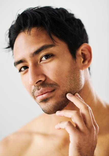Skincare routine, skin and grooming done by a man against a white studio background. Portrait of one Asian male with soft, silky and smooth facial skin showing, touching and looking at his beard stock photo