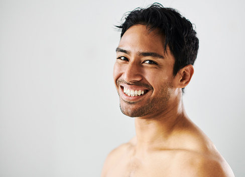 Happy, smiling and cheerful man showing off his perfect white teeth and bright smile while standing against a studio background. Portrait of the face of a young and joyful man showing his clear skin