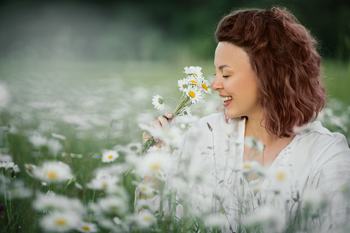 Young beautiful happy woman enjoying flowers in beautiful chamomile field. Summertime.