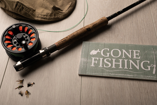 Gone fishing, fly fishing rod and reel on a light wood background