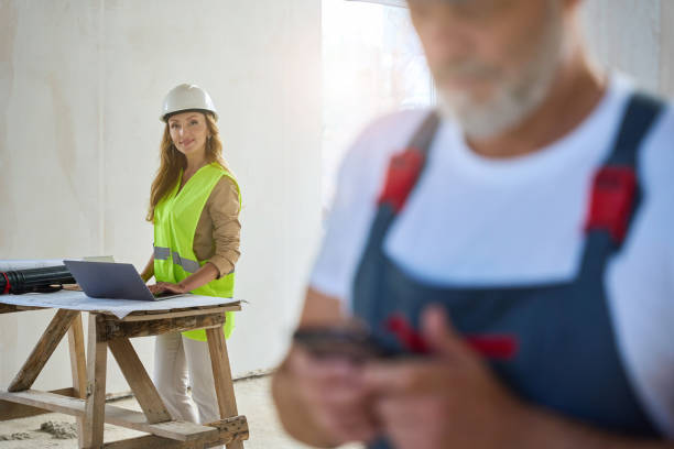 istock Cropped photo of builder in overalls typing message on mobile 1412474545