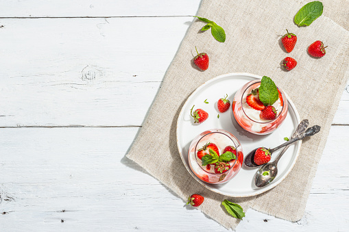 Italian dessert panna cotta in glass with strawberries. Healthy sweet food, trendy hard light, dark shadow. Rustic style concept, white wooden boards background, top view