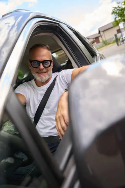 Adult man in glasses sits in a car with an open window. Cropped photo