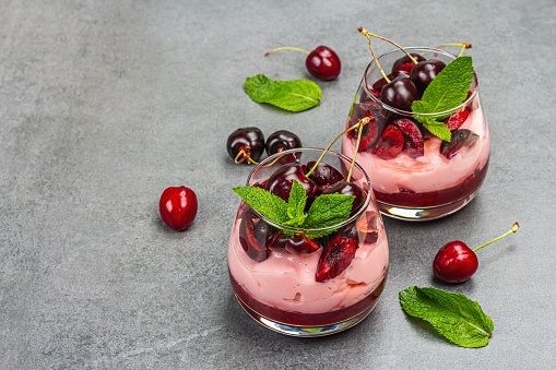 Delicious Italian dessert panna cotta with sweet cherry sauce, fresh berries and mint leaves. Stone concrete background, copy space