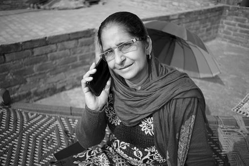 Rural Indian mature woman sitting on rooftop and she talking on mobile phone.