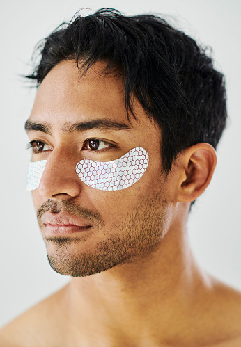 Under eye, face and skincare patches applied on a man with a studio background. Anti aging collagen patch to male eye or cheeks for a younger, fresh and clean looking skin. Male facial care routine