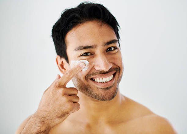 istock Man applying face cream or lotion during skincare routine against grey background with copy space. Portrait of a handsome, confident young male grooming and enjoying hygienic self care after a shower 1412485978
