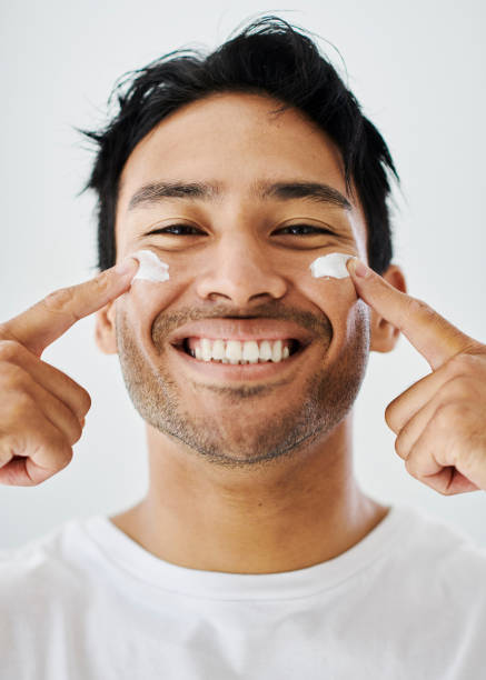 Skincare, healthy skin and face routine using moisturizer to achieve a flawless complexion. Portrait of handsome and happy male smiling while using facial cream practicing good hygiene and selfcare