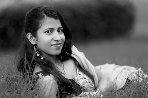 Monochrome image of young Indian girl laying in grass outdoors in the public park.