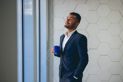 black man working in an office, holding a coffee mug on his break