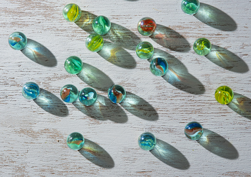 Colorful glass marbles with sun reflection, light and shadow on wooden background