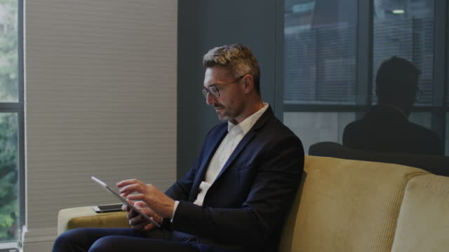 Businessman watching, reading and looking at funny video on tablet while on a business break. One mature modern corporate man typing, interacting and enjoying online on social media in his free time