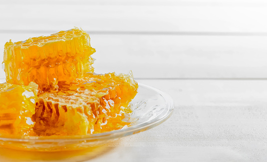 Honeycomb with fresh honey on a glass plate. White wooden background. Copy space.