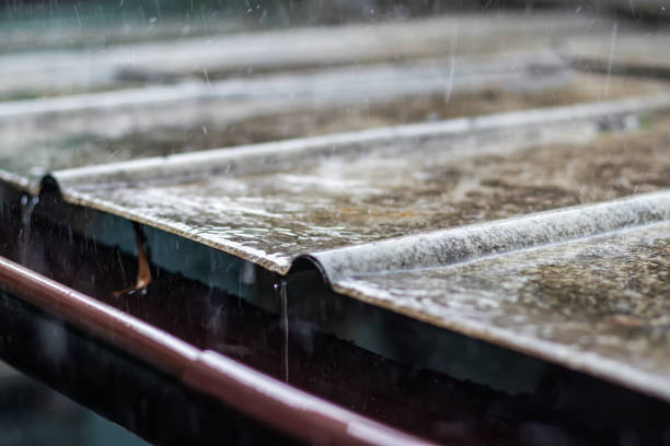 Rain water is pouring from the green draining gutter on the pavement, selective focus