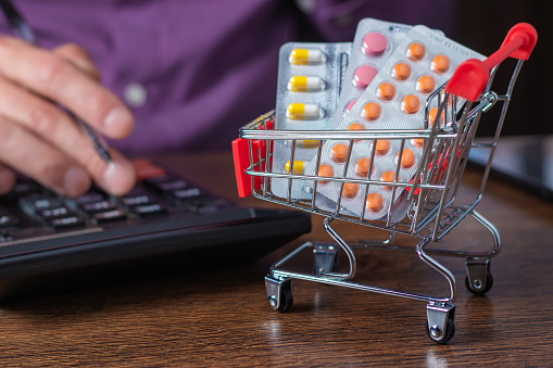 Concept of large spending on medicines. Shopping cart full of medicines and pills. A man calculates the cost of medicines on a calculator.