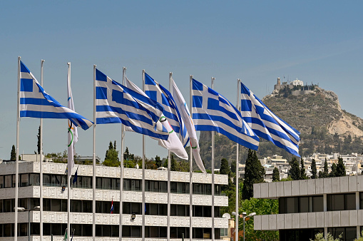 Athens, Greece - May 2022: Scenic view of Greek national flags flying at the city's historic Olympic Stadium with Lycabettus Hill in the distance