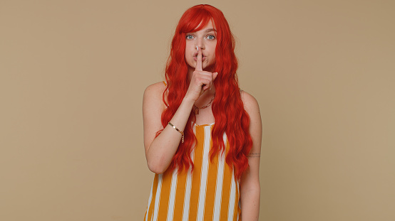 Shh be quiet please. Portrait of redhead woman 20s presses index finger to lips makes silence gesture sign do not tells secret. Young beautiful ginger girl posing isolated on beige studio background