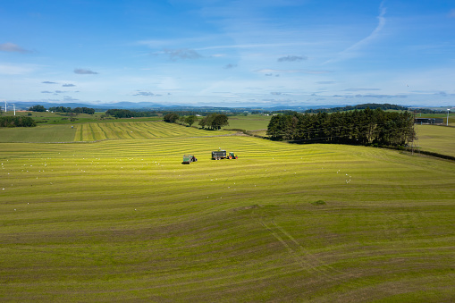 Drone view of tractors working in a field collecting cut grass in rural south west Scotland