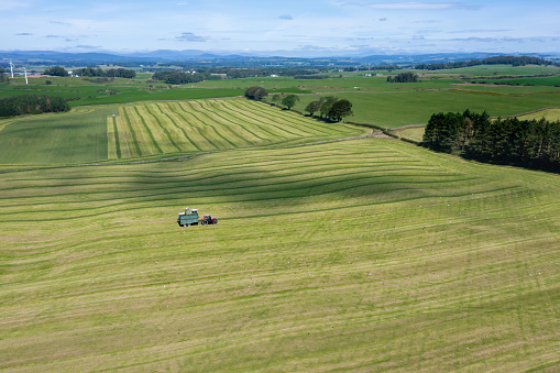 Drone view of tractors working in a field collecting cut grass in rural Dumfries and Galloway Scotland
