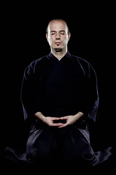 portrait of a kendo fighter meditating, against black backgroung