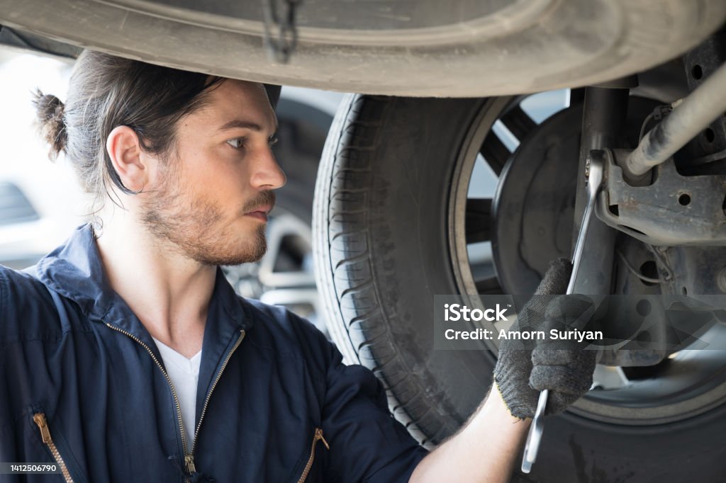 Mechanic checking maintenance car engine underneath lifted car. Mechanic vehicle using wrench tool for maintenance car at automative motor garage 20-24 Years Stock Photo