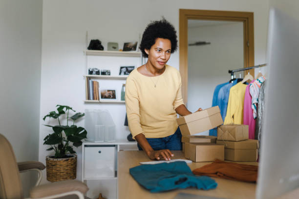 istock African Businesswoman using computer while packing clothes in a cardboard box 1412516980