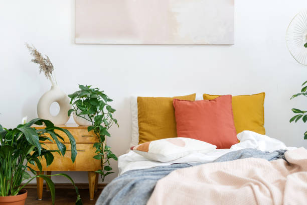 istock Bed with crumpled plaid, cushions, side table and houseplants 1412516989
