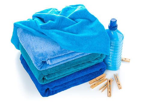 High angle view of a stack of three blue towels isolated on white background. A blue plastic bottle of laundry detergent or and fabric softener and clothespin complete the composition. High resolution 42Mp studio digital capture taken with Sony A7rII and Sony FE 90mm f2.8 macro G OSS lens