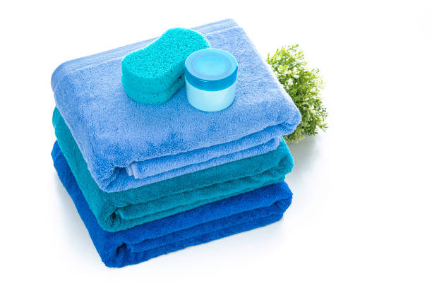 High angle view of a stack of three blue towels isolated on white background. A bath sponge and soap complete the composition. High resolution 42Mp studio digital capture taken with Sony A7rII and Sony FE 90mm f2.8 macro G OSS lens