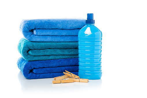 Close up view of a stack of three blue towels isolated on white background. A blue plastic bottle of laundry detergent or and fabric softener and clothespin complete the composition. High resolution 42Mp studio digital capture taken with Sony A7rII and Sony FE 90mm f2.8 macro G OSS lens