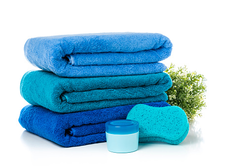 Close up view of a stack of three blue towels isolated on white background. A bath sponge and soap complete the composition. High resolution 42Mp studio digital capture taken with Sony A7rII and Sony FE 90mm f2.8 macro G OSS lens