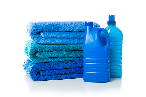 Close up view of a stack of three blue towels isolated on white background. Plastic bottles of laundry detergent and fabric softener complete the composition. High resolution 42Mp studio digital capture taken with Sony A7rII and Sony FE 90mm f2.8 macro G OSS lens