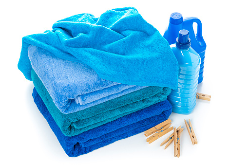 High angle view of a stack of three blue towels isolated on white background. Plastic bottles of laundry detergent and fabric softener complete the composition. High resolution 42Mp studio digital capture taken with Sony A7rII and Sony FE 90mm f2.8 macro G OSS lens