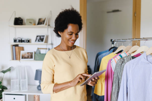 istock Afro Businesswoman using digital tablet while packing clothes in a cardboard box 1412520073