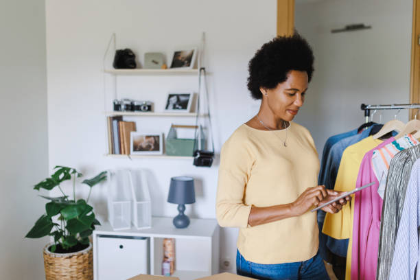 istock Afro Businesswoman using digital tablet while packing clothes in a cardboard box 1412520112