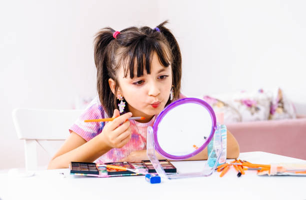 istock little girl applying make-up and looking at her reflection in mirror while sitting at the dressing table 1412524707