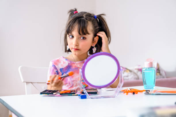 istock little girl applying make-up and looking at her reflection in mirror while sitting at the dressing table 1412524710